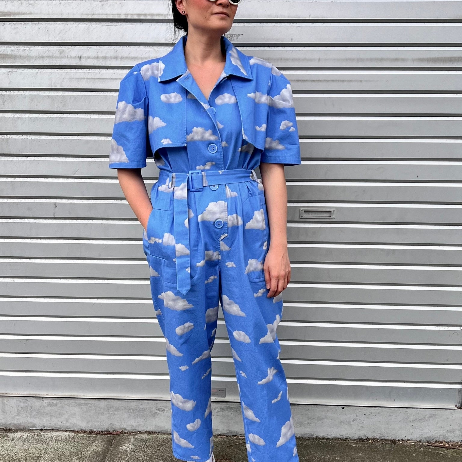 Person wearing a blue jumpsuit with cloud pattern standing in front of a gray wall.