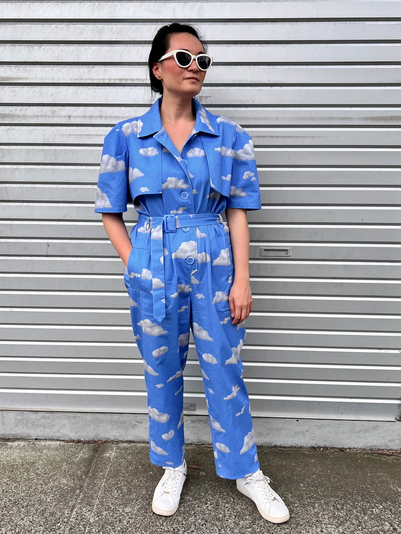 Person wearing a blue jumpsuit with cloud pattern standing in front of a gray wall.