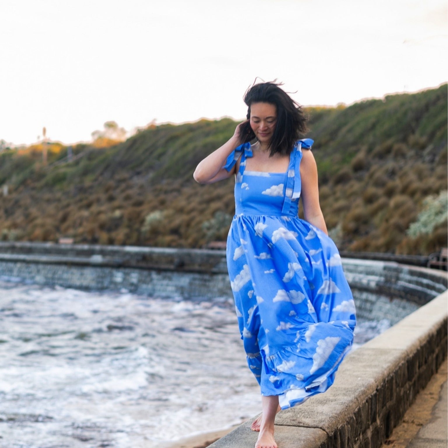 Woman in a blue dress with cloud pattern standing by a the ocean