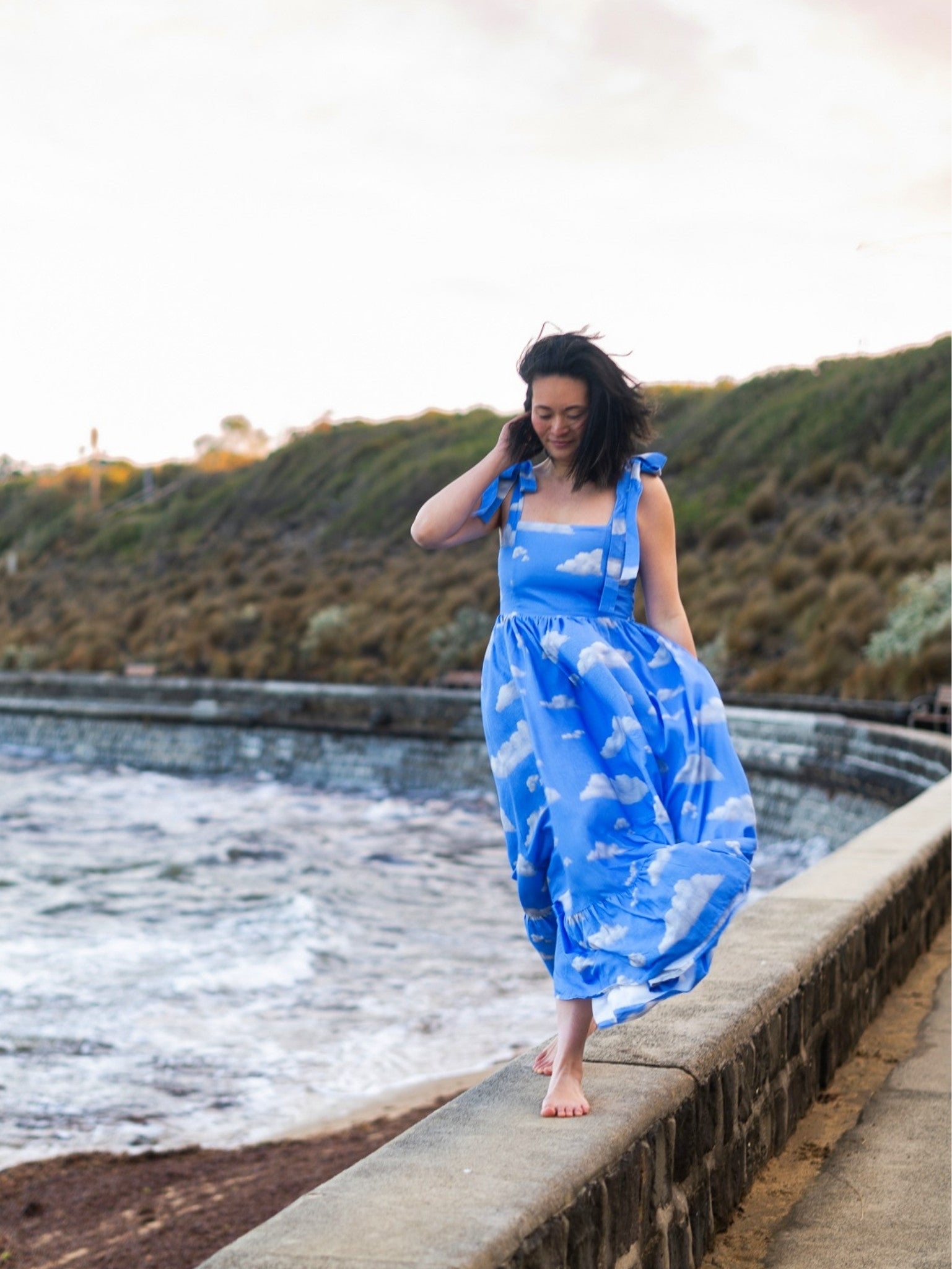 Woman in a blue dress with cloud pattern standing by a the ocean