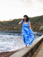 Woman in a blue dress with cloud pattern standing by a the ocean